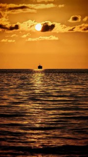 Single ship in golden sunlight reflecting romantically on the calm sea under a clear sky, Batumi,