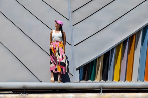 A woman stands confidently against a backdrop of modern architecture, her colorful outfit creating