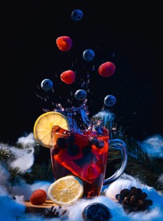 Raspberries and blueberries fall into a glass cup with punch, winter atmosphere, dark background