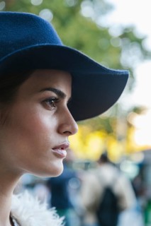 A side profile of a thoughtful woman wearing a fashionable hat, set against a softly blurred
