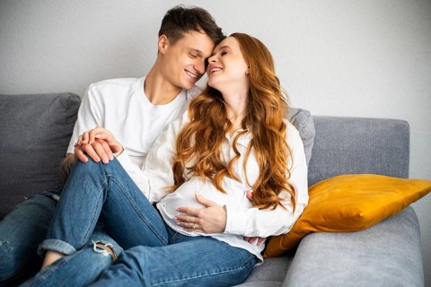A joyful young couple lovingly embraces on a comfortable sofa, eagerly anticipating the arrival of