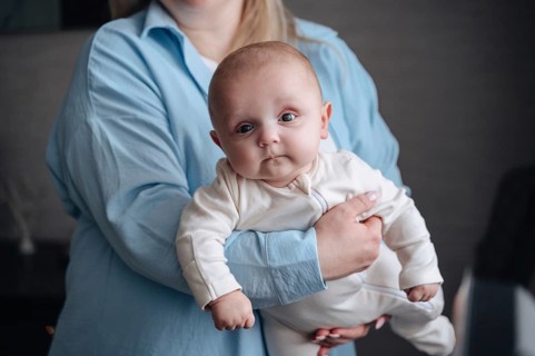 A cute baby boy gazes curiously while being held gently by his mother. The intimate setting conveys