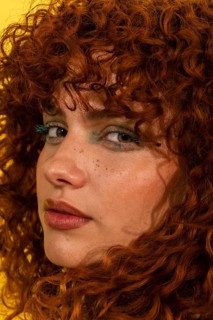 A striking portrait of a woman with curly red hair. Her expressive eyes, accentuated by bold