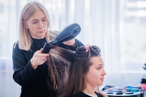 A hair stylist uses a hair dryer to dry a woman's hair during a keratin hair straightening
