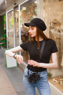 A young woman, equipped with a camera, checks her watch while strolling through a vibrant city