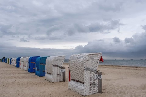Row of white and blue beach chairs on the beach under a cloudy grey sky, Föhr, Nordfriesland,