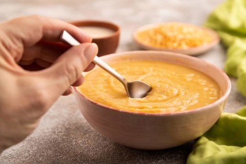 Pea cream soup, Puree, porridge in ceramic bowl with hand on brown concrete background and green