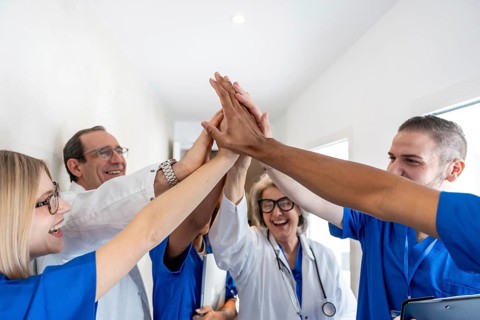 Diverse group of smiling healthcare professionals creating a high five gesture in a hospital