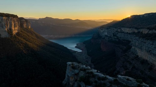 A breathtaking view of the Panta de Sau Reservoir at sunset, surrounded by steep cliffs and lush