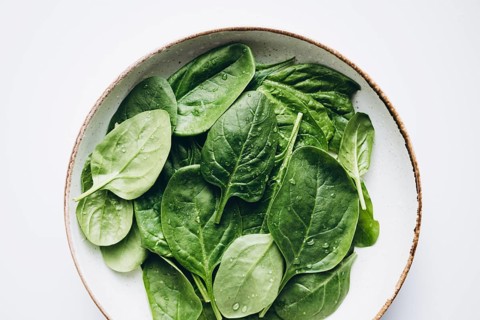A bowl filled with fresh green spinach leaves, glistening with water droplets. Capturing their