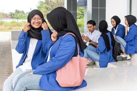 A group of Asian Muslim students socialize on a university campus in casual attire. They prepare