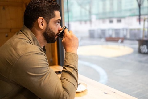 A man in a cafe enjoys a warm coffee, gazing outside on a rainy day in the city. The serene