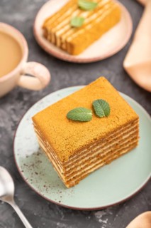 Homemade honey cake with milk cream and mint with cup of coffee on a black concrete background and