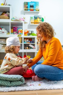 Vertical photo of a cute girl and mother playing nurses sitting on the floor at home