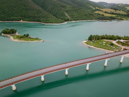 A serene aerial view of a bridge stretching across the calm waters of Castreccioni Lake in Italy.