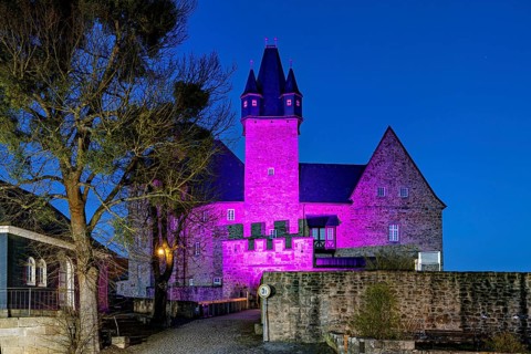 View of a castle ruin at night, illuminated by pink and violet light, Spangenberg Castle