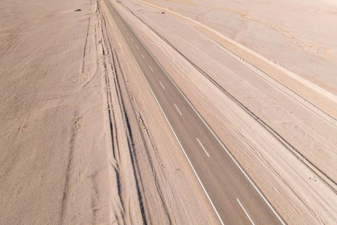 Aerial view of a long, straight road cutting through a vast, barren desert landscape in the