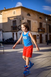 Young child rollerblading on a cobblestone street in a scenic village, wearing a blue and red