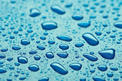A striking close up image showcasing glistening blue water droplets on a textured surface. The