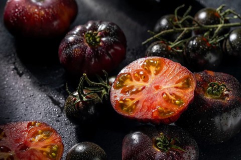 A collection of ripe heirloom tomatoes with rich colors, glistening with water droplets on a dark