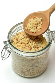 Fregola in wooden spoon and glass container, pasta variety from Sardinia, Italy