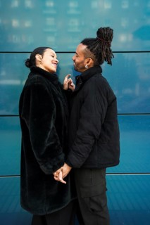A multiethnic couple stands outdoors in cozy jackets, sharing a joyful moment as they smile warmly