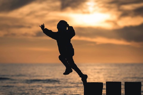 Silhouette of boy jumping from breakwater stilt during sunset in Poland