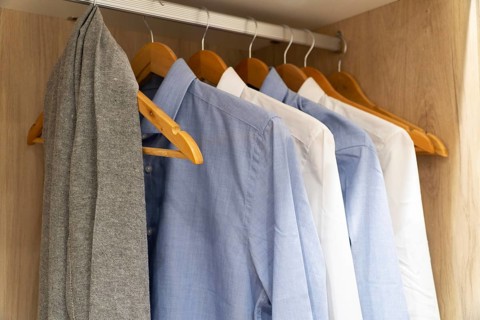 A selection of blue and white shirts, hangs neatly on wooden hangers in a wooden closet. The scene