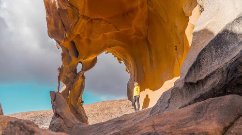 A woman stands beneath a striking natural arch formation in a rugged desert landscape in