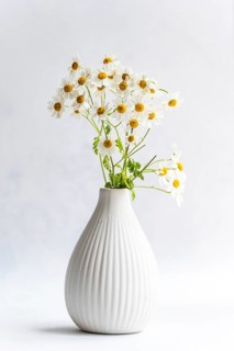 A collection of delicate daisies beautifully arranged in a white, textured vase against a soft,