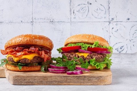 Two burgers with beef patty, fried bacon, cheddar cheese, tomatoes, on a light table