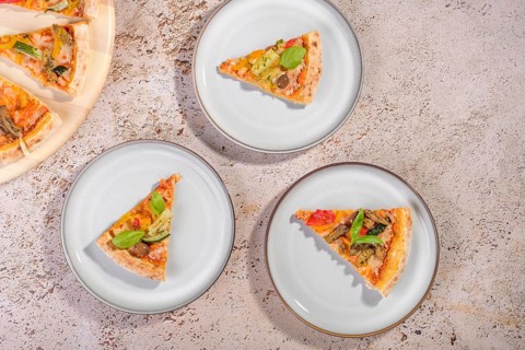 A vibrant display of vegetarian pizza slices topped with fresh basil, zucchini, and eggplant on