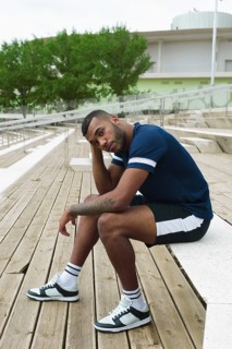 A black male athlete in sporty attire sits on wooden steps, taking a break from training. He