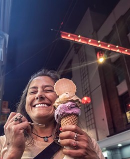 A woman joyfully holding an ice cream cone in a lively Melbourne street at night, under bright