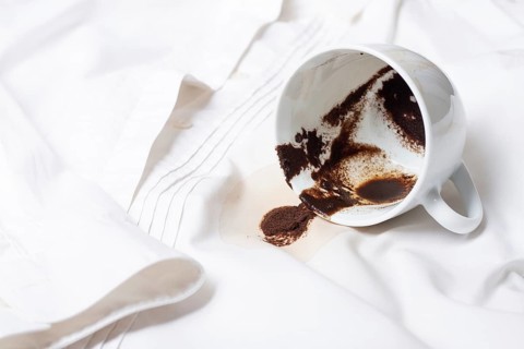 A white cup with the remains of coffee, spilled, lies on a white shirt, there are no people, a soft