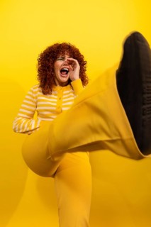A joyful woman dressed in bright yellow clothing, energetically kicking and laughing against a