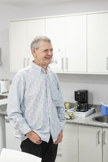 A man with intellectual disabilities stands smiling in a bright, modern kitchen with light cabinets