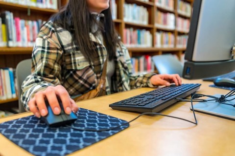 Student hands typing on keyboard and operating mouse at a desktop computer, focusing on online