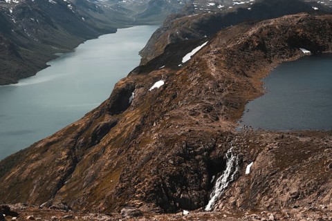A breathtaking view of a cascading waterfall flowing into a mountain lake in Norway Surrounded by
