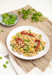 Quinoa porridge with green pea, corn and dried tomatoes on ceramic plate on a white wooden