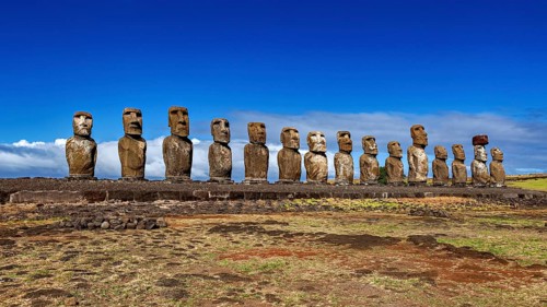 Moai statues stand in a long line against a clear sky on a grassy area, The Moai statues on Easter