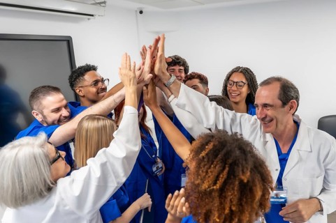 Diverse medical professionals and students uniting hands in a meeting room, symbolizing teamwork,