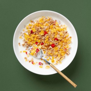 Top view of a nutritious bowl of cereals mixed with milk and colorful fruits on a green background.