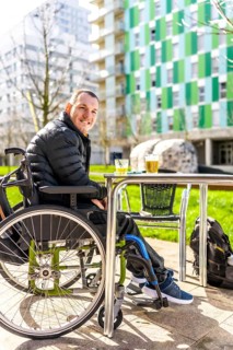 Young man in a wheelchair enjoys a refreshing drink with a friend at an outdoor cafe in the city,