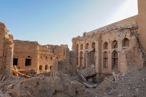 Weathered and crumbling structures in Al Hamra, an abandoned clay village, against a clear blue sky