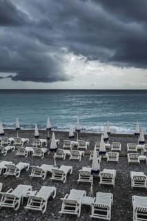 White reclining chairs on deserted beach during bad weather with dark, menacing rain clouds over