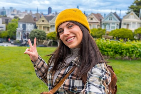 Young woman smiling and holding up two fingers for a peace sign, enjoying her urban vacation with