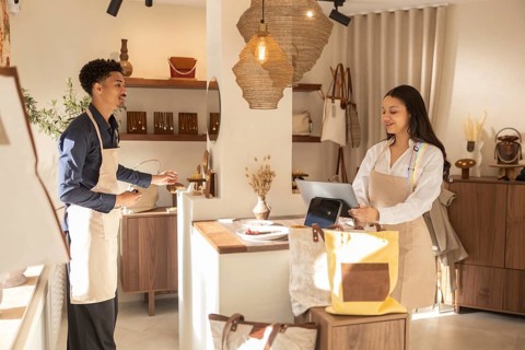 Two staff member converse in a stylish bag store. The store interior showcases a variety of bags,