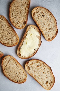 Top view of sliced fresh homemade sourdough bread with some slices generously spread with butter,