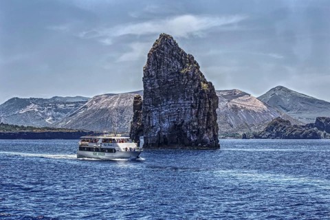 A large rock massif juts out of the blue sea, a ship sails past it, Lipari Aeolian Islands, Sicily